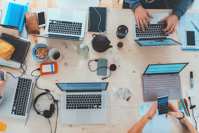 Birds eye view of a group of people sitting at a table using social media on phones and computers.